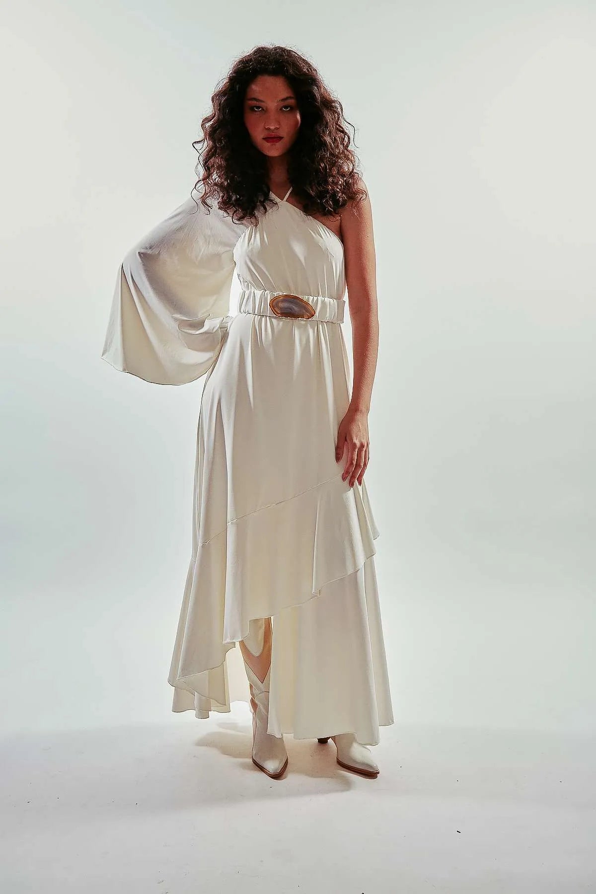 Vestido largo liso y asimétrico de una manga larga, color blanco, con vuelo y volantes