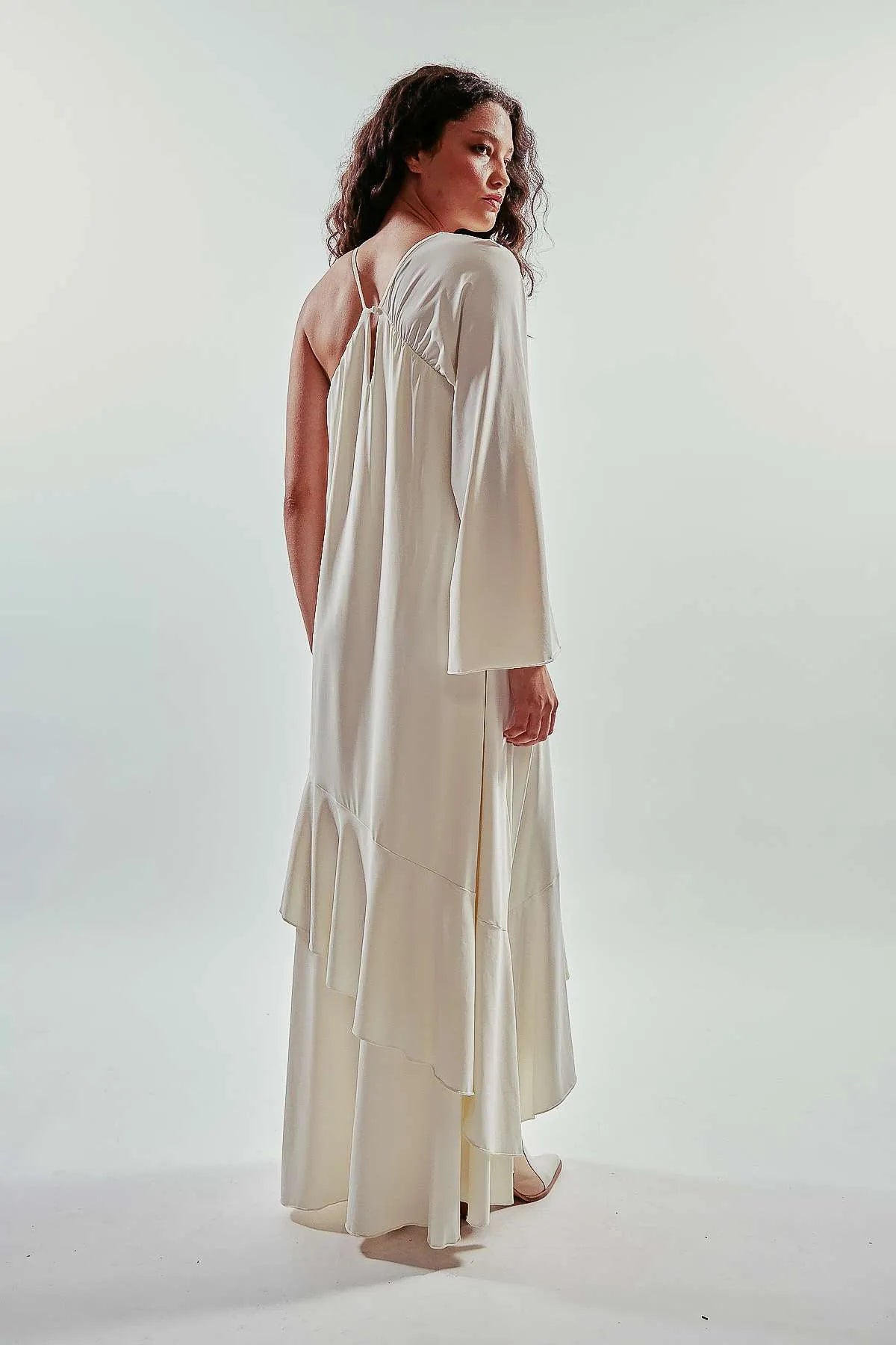 Vestido largo liso y asimétrico de una manga larga, color blanco, con vuelo y volantes